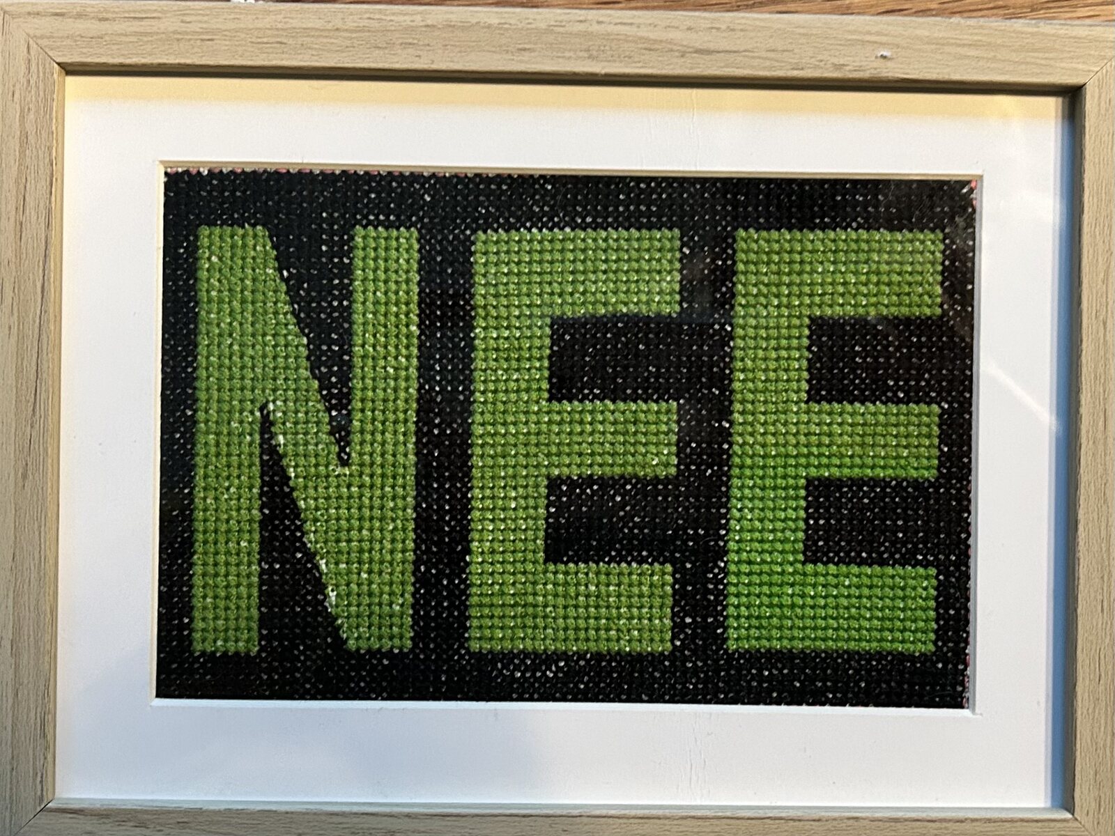 Ingelijst groen borduurwerk met de tekst NEE